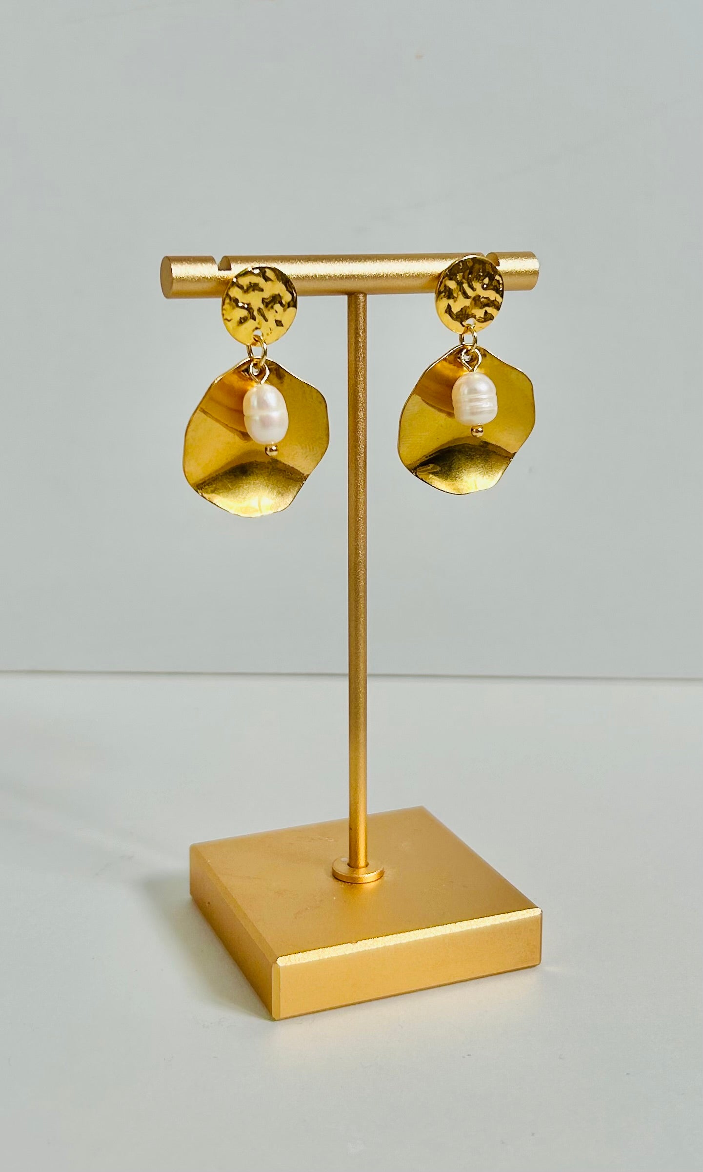 Gold earrings on a matching gold stand against a light gray background