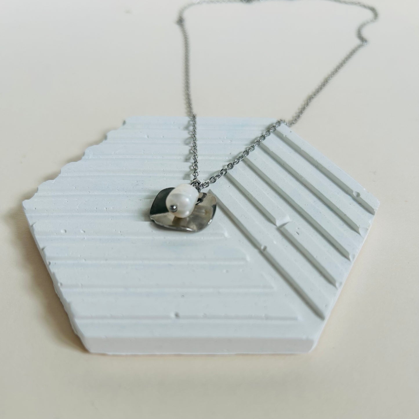 Silver necklace with a pearl pendant on a white hexagonal stand