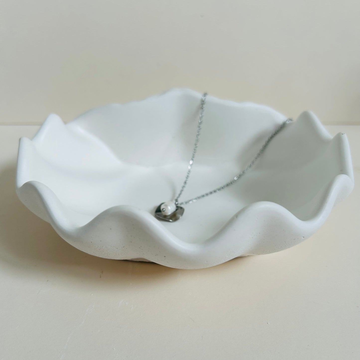 White ceramic dish with a necklace on a light gray background