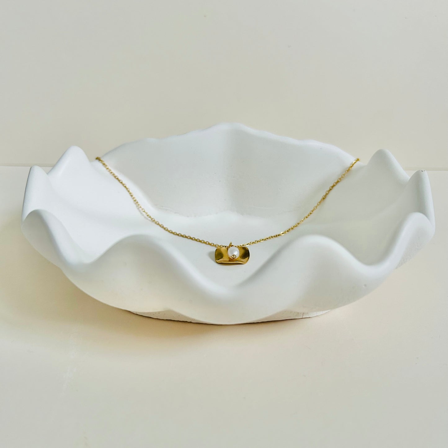 White ceramic dish with a gold necklace draped over it on a beige background