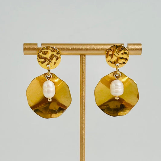 Gold earrings with a pearl center on a gold stand against a light gray background