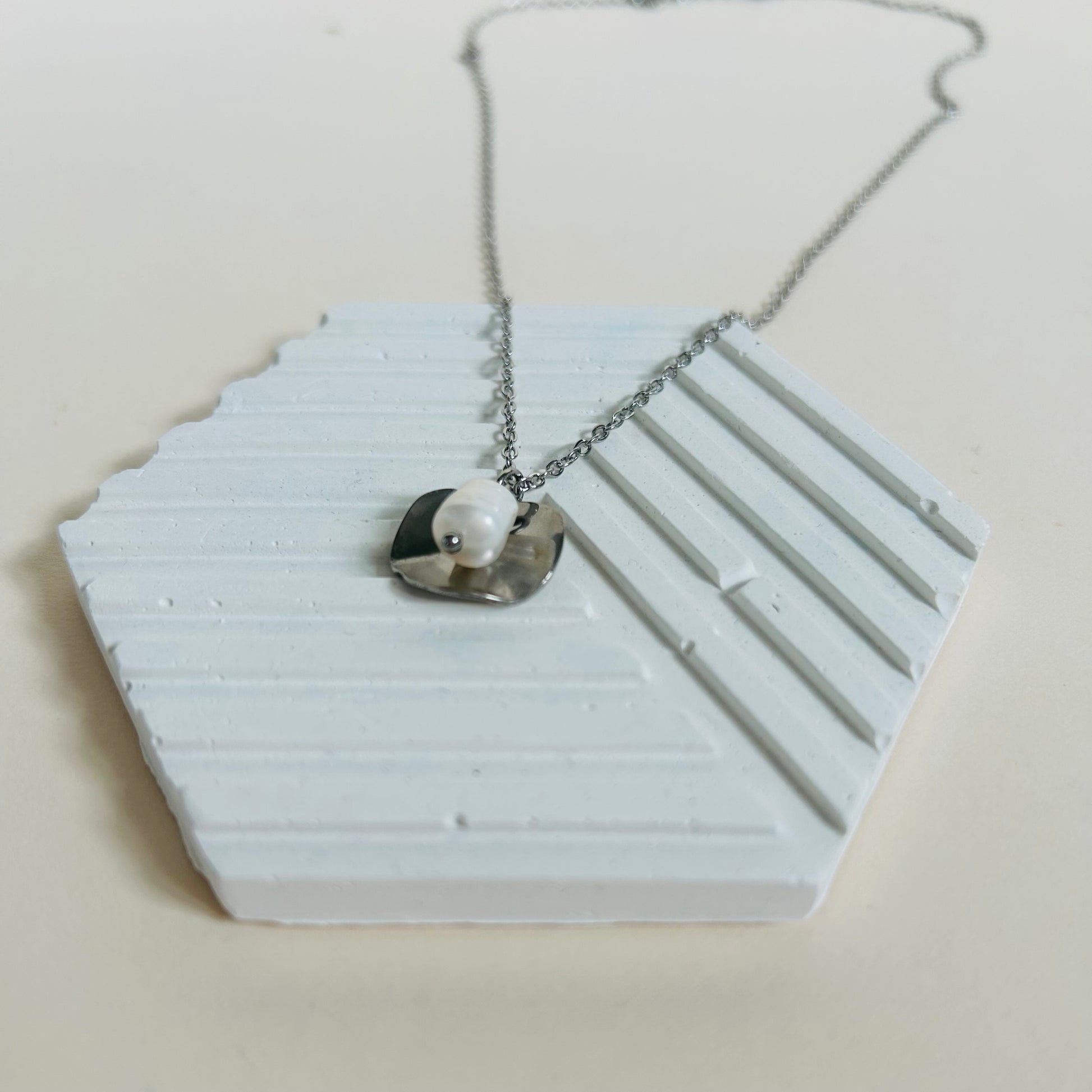 Silver necklace with a pearl pendant on a white hexagonal stand