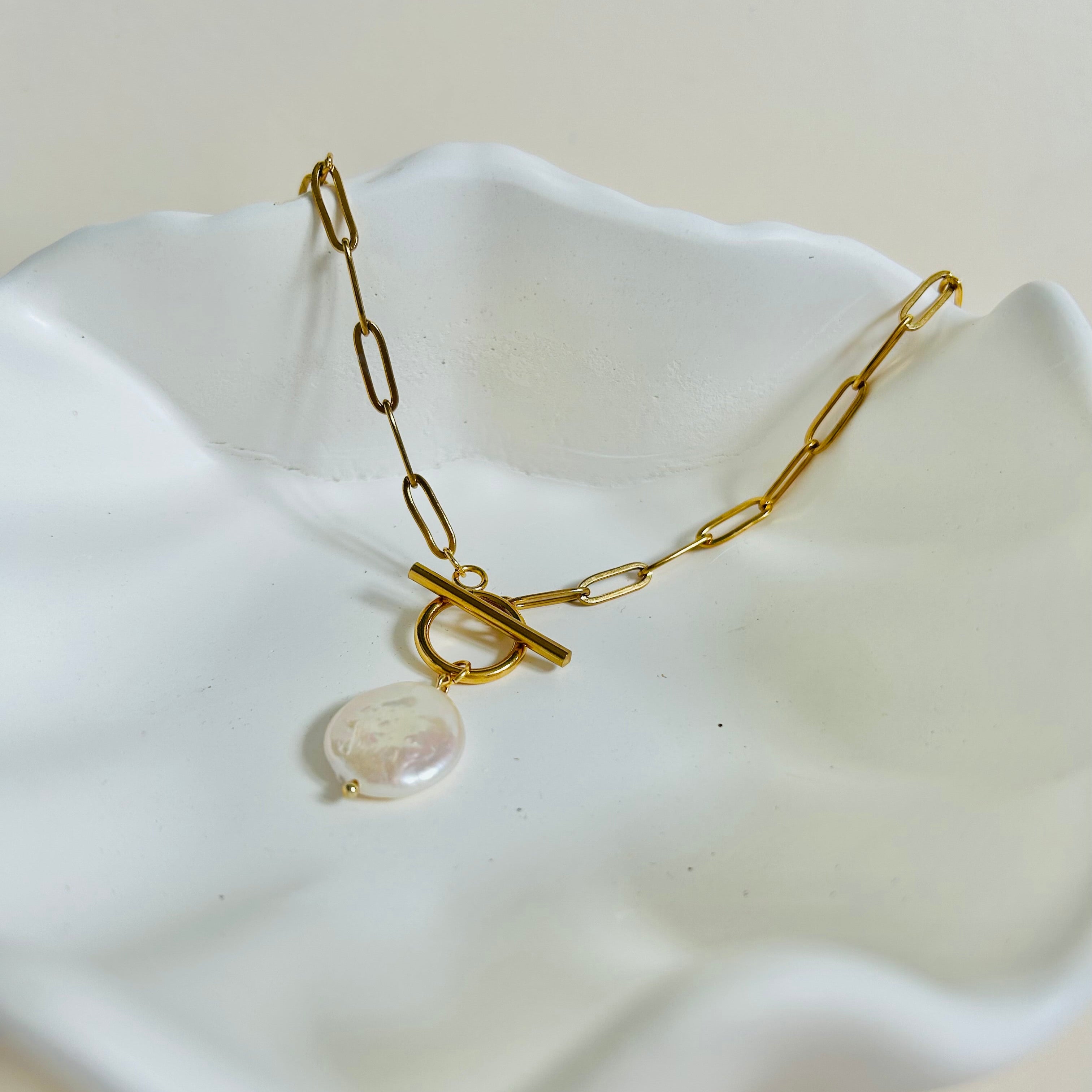 Gold necklace with a round pendant on a white dish