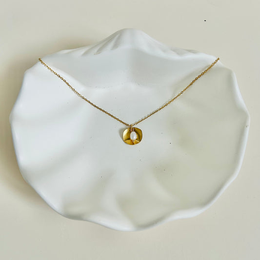 Gold necklace with a pendant on a white dish against a beige background