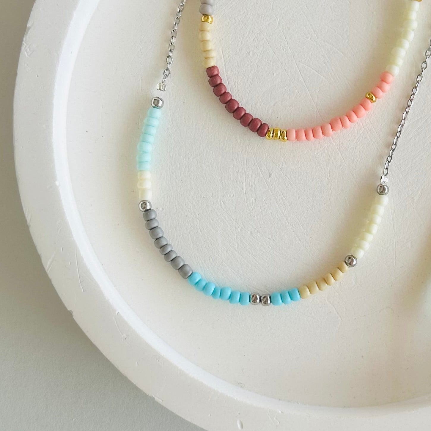 Three beaded necklaces on a white dish with a light gray background