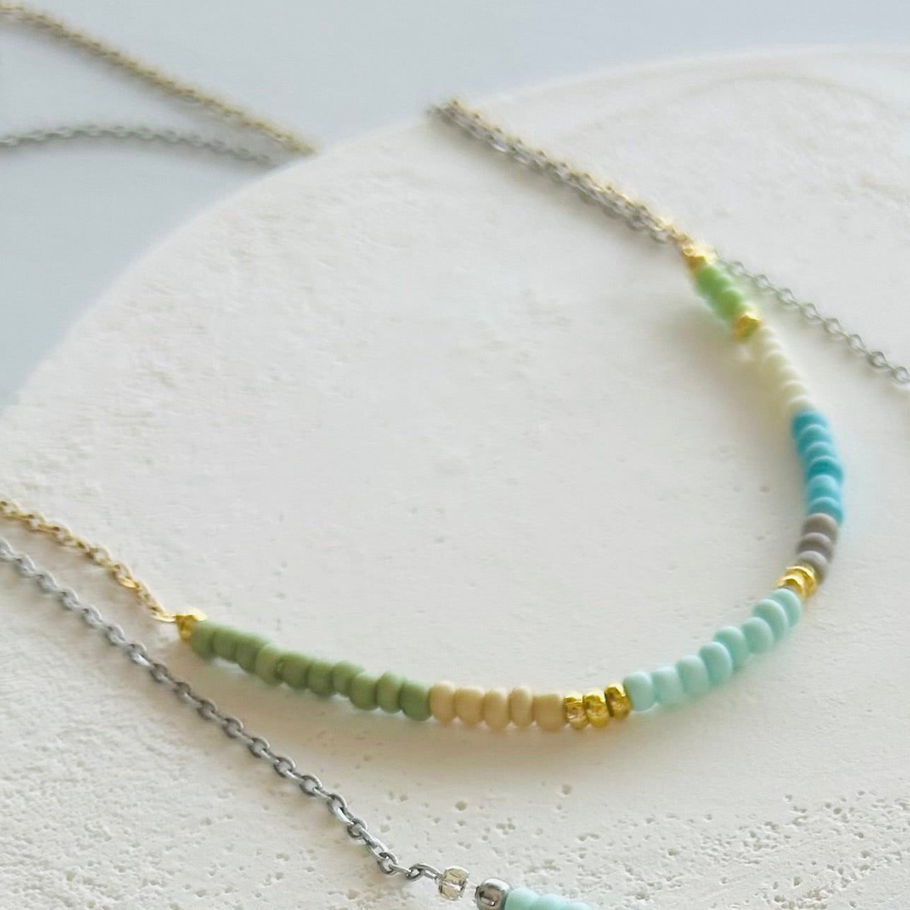 Two beaded necklaces on a round white stone surface