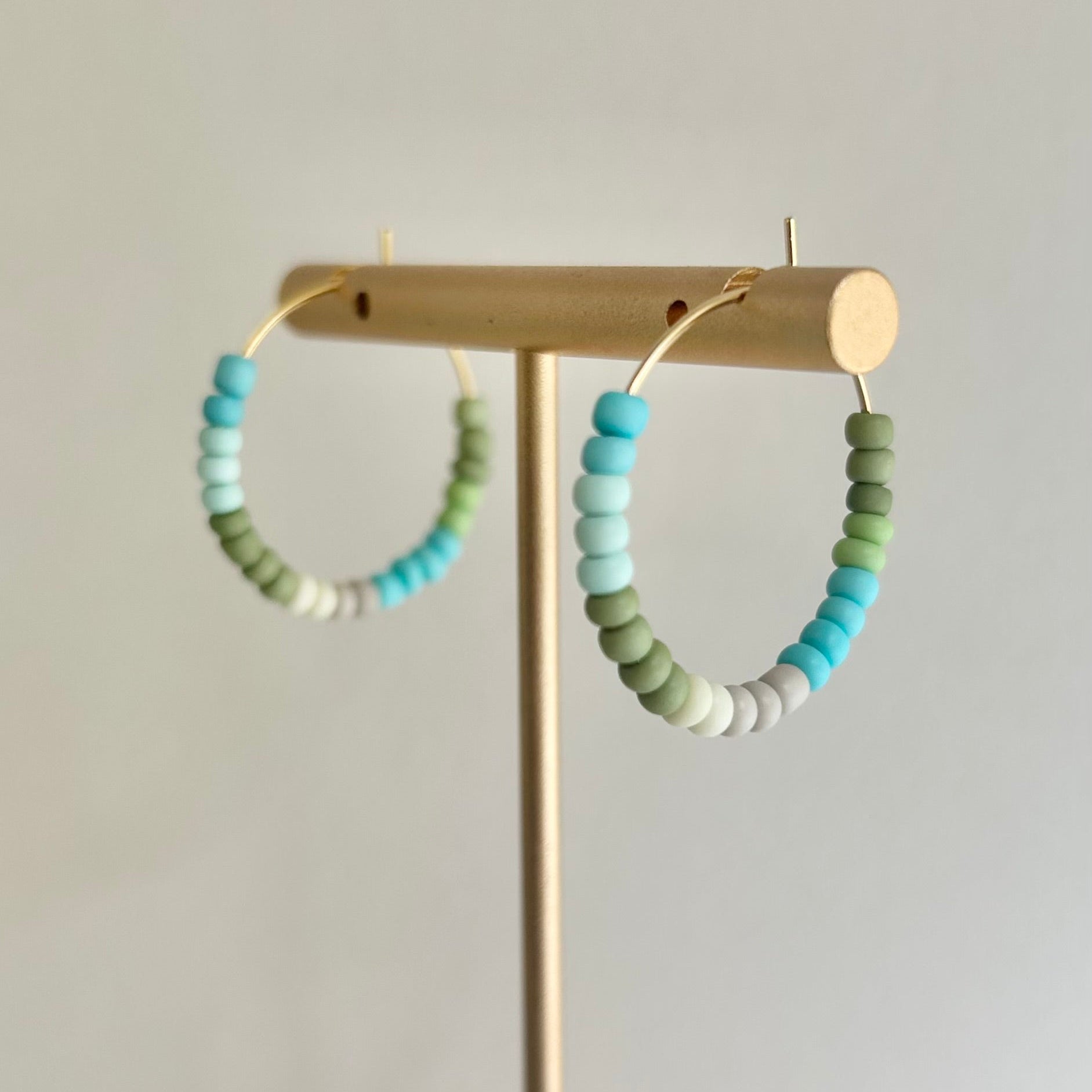 Pair of beaded hoop earrings on a gold stand against a light gray background