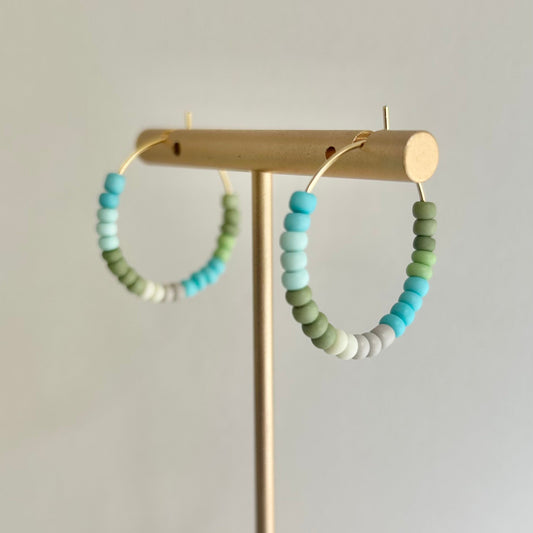 Pair of beaded hoop earrings on a gold stand against a light gray background