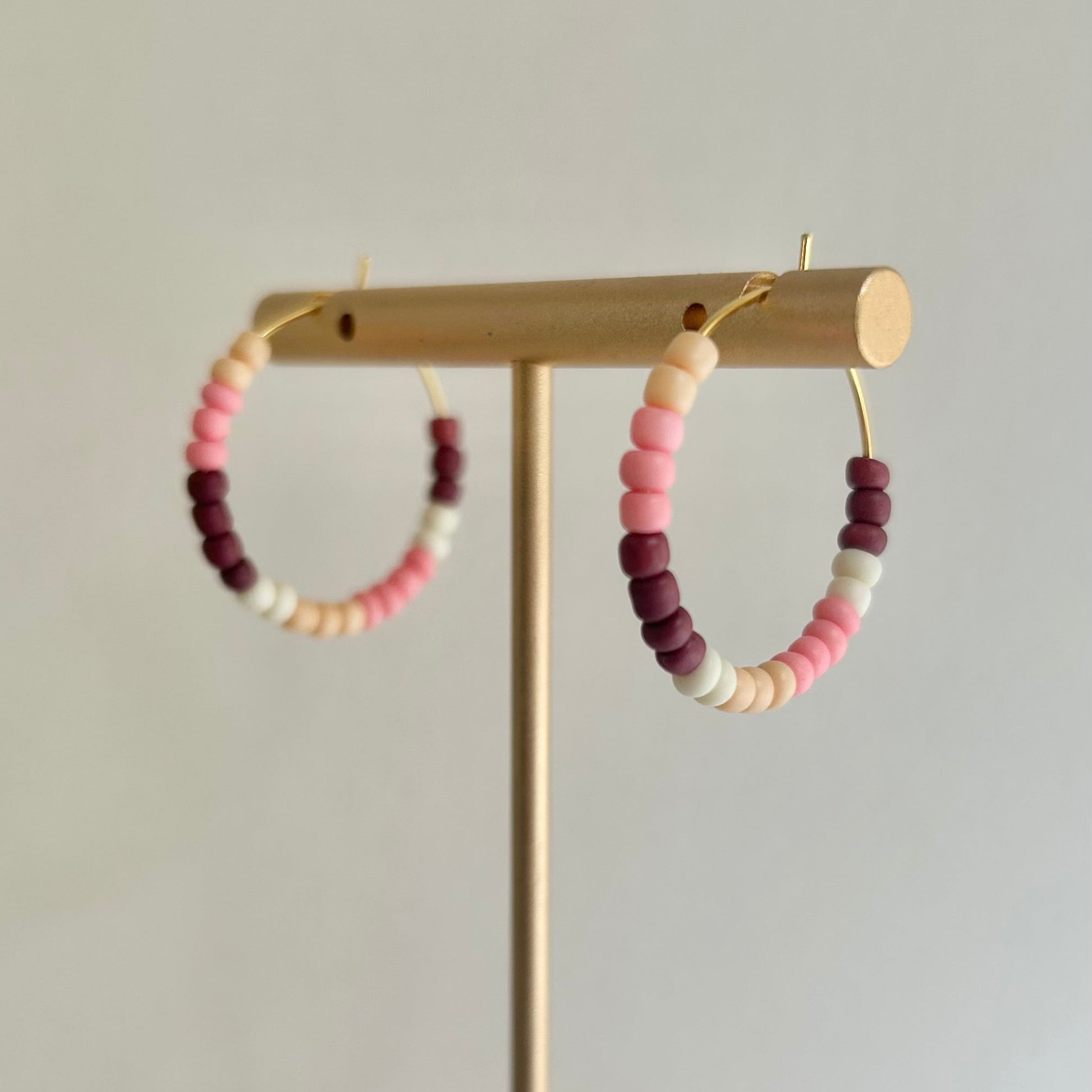 Colorful beaded hoop earrings on a wooden stand against a plain background