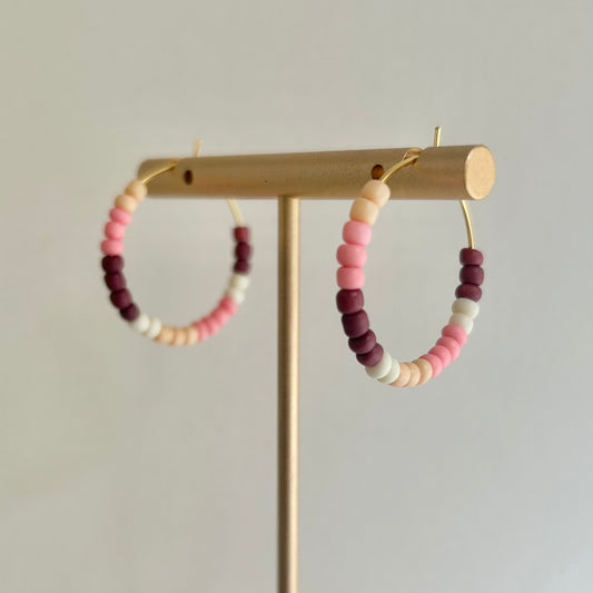 Colorful beaded hoop earrings on a wooden stand against a plain background