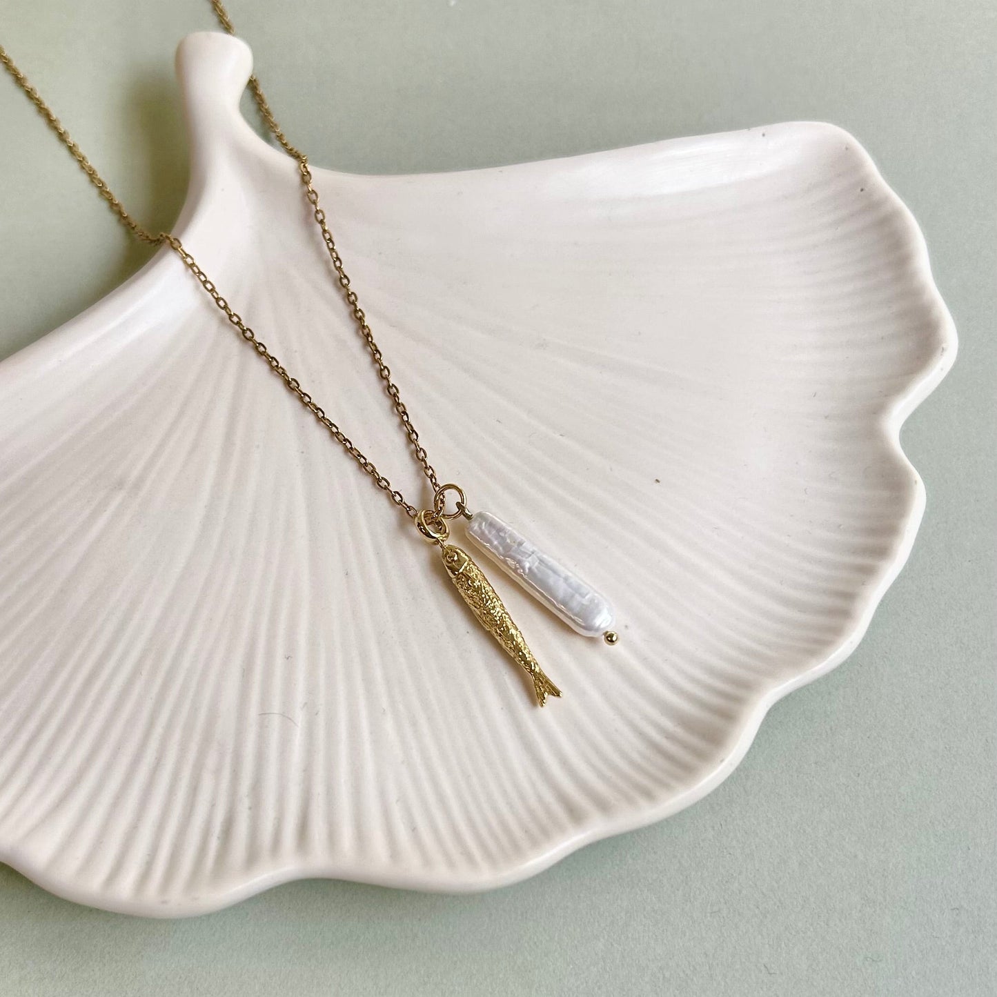 Necklace with a pearl & fish pendant on a white shell against a light green background