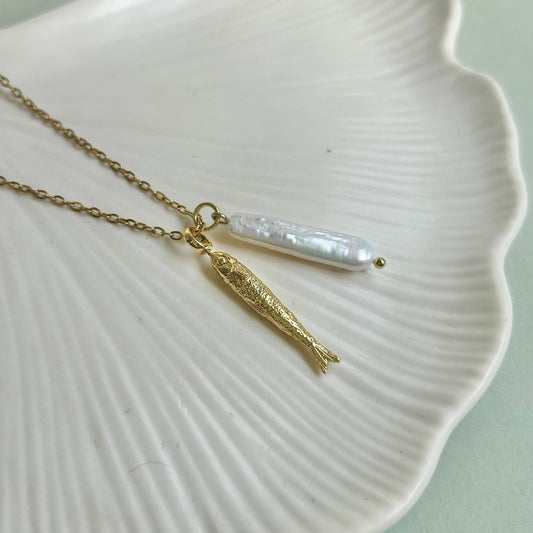 Gold necklace with a pearl pendant and fish on a white shell against a light green background
