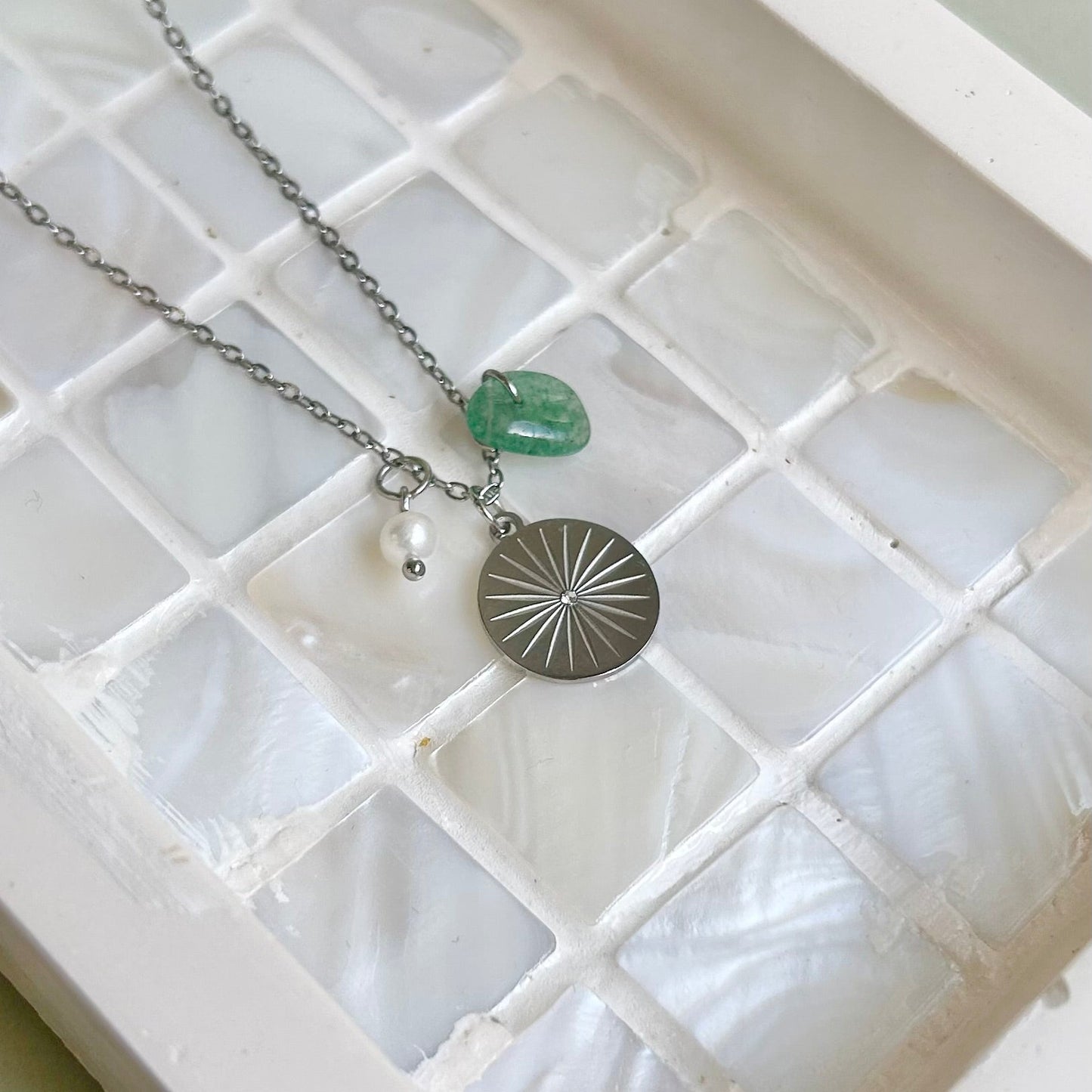 Necklace with green pendant and pearl on a white textured surface