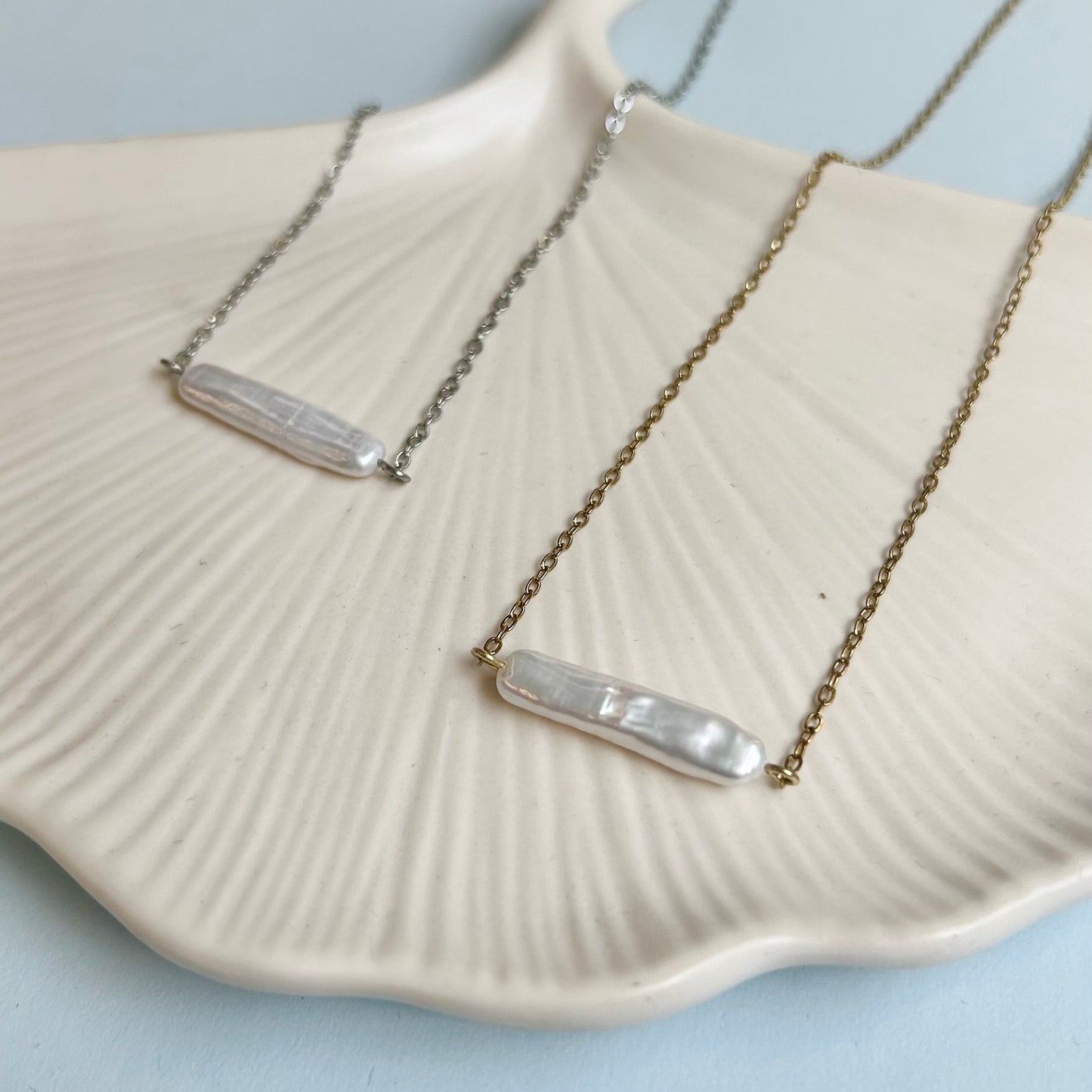 Two baroque pearl stick necklaces on a shell with a light blue background